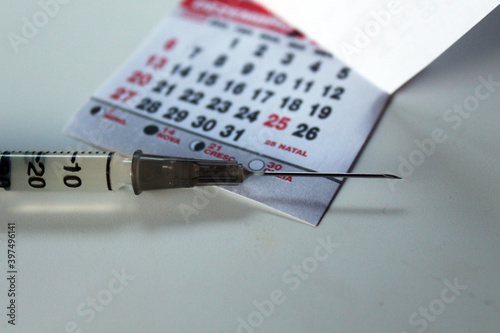 Close up of syringe and a calendar.
