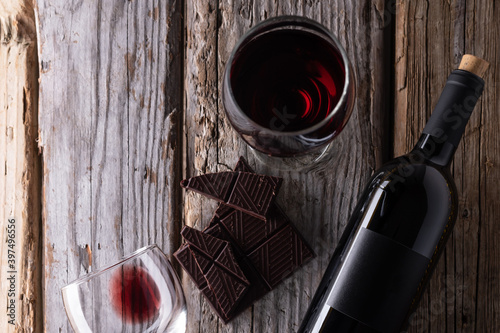 View from above of elegant bottle and wineglasses of red wine with dark chocolate on rustic wooden background. Wine and dessert. Template concept for your design and advertising company promotion.