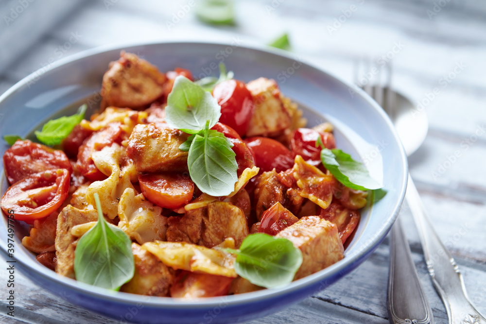 Farfalle pasta with chicken breast, cherry tomatoes and fresh basil. Bright wooden background. Close up. Farfalle pasta with chicken breast, cherry tomatoes and fresh basil. Bright wooden background. Close up.