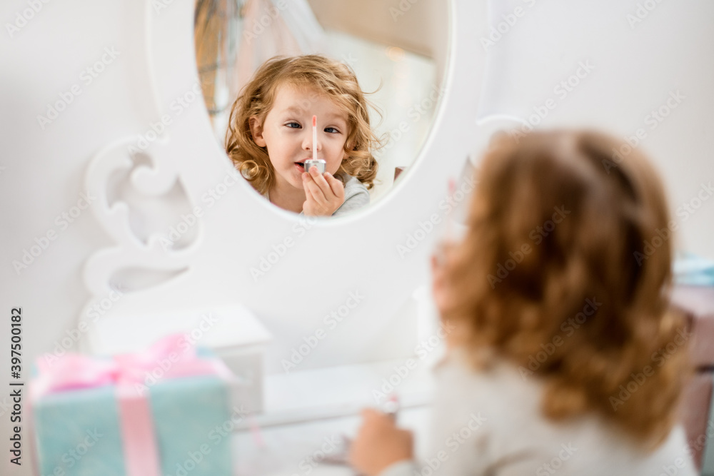 Reflection in the mirror of little girl holding lip gloss brush in front of her Reflection in the mirror of little girl holding lip gloss brush in front of her