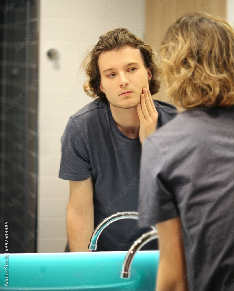 young man looking in the mirror,combing his hair,looking at problems on face. young man looking in the mirror,combing his hair,looking at problems on face.