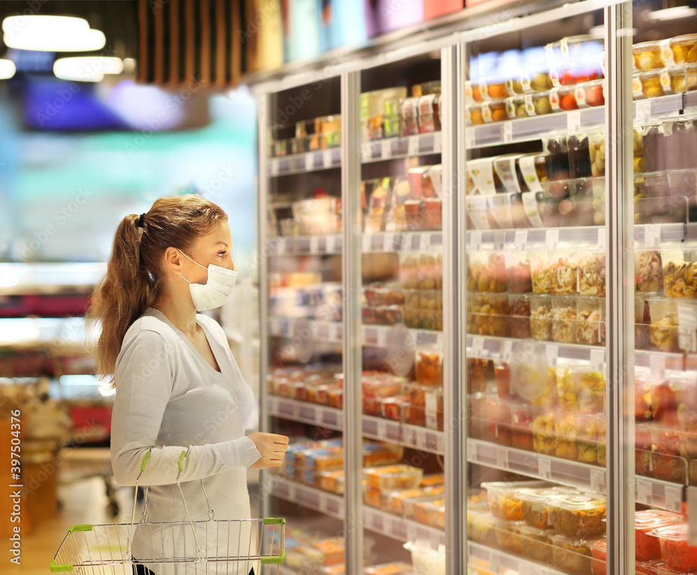 Woman choosing frozen food from a supermarket freeze.Supermarket shopping, face mask 
