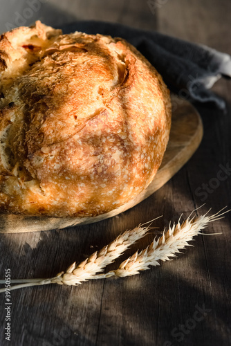 The handcrafted tartin bread lies on a wooden surface next to wheat ears. Farming and home baking concept