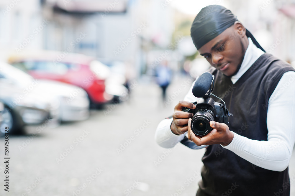 Young professional african american videographer holding professional camera with pro equipment. Afro cameraman wearing black duraq making a videos.