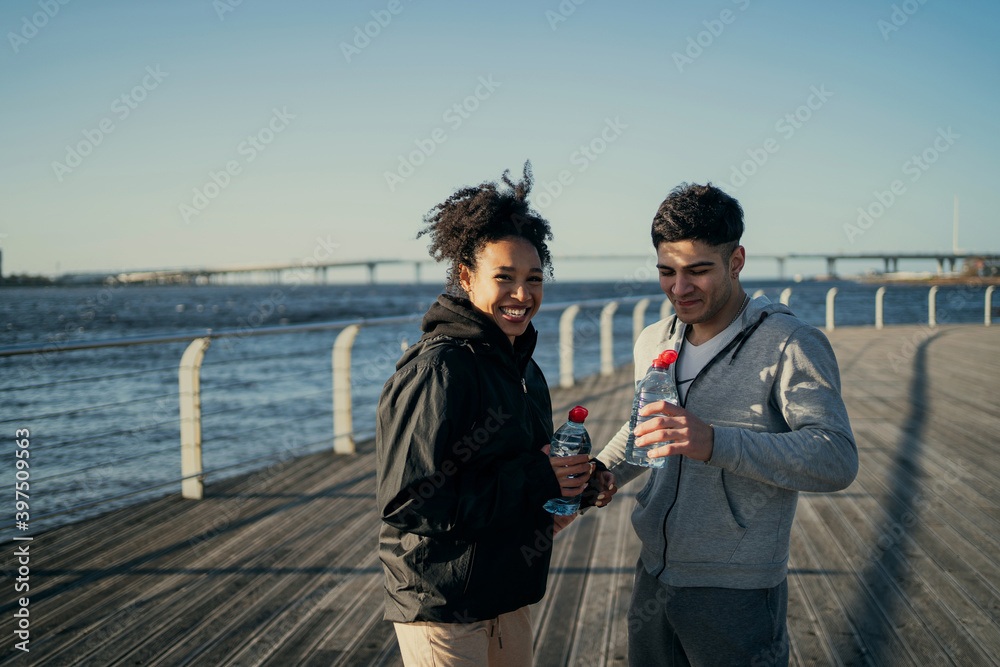 sports fitness an African-American woman and a Latin man in comfortable street clothes for sports. a sporty couple drink water during a morning jog in the city's Central Park.