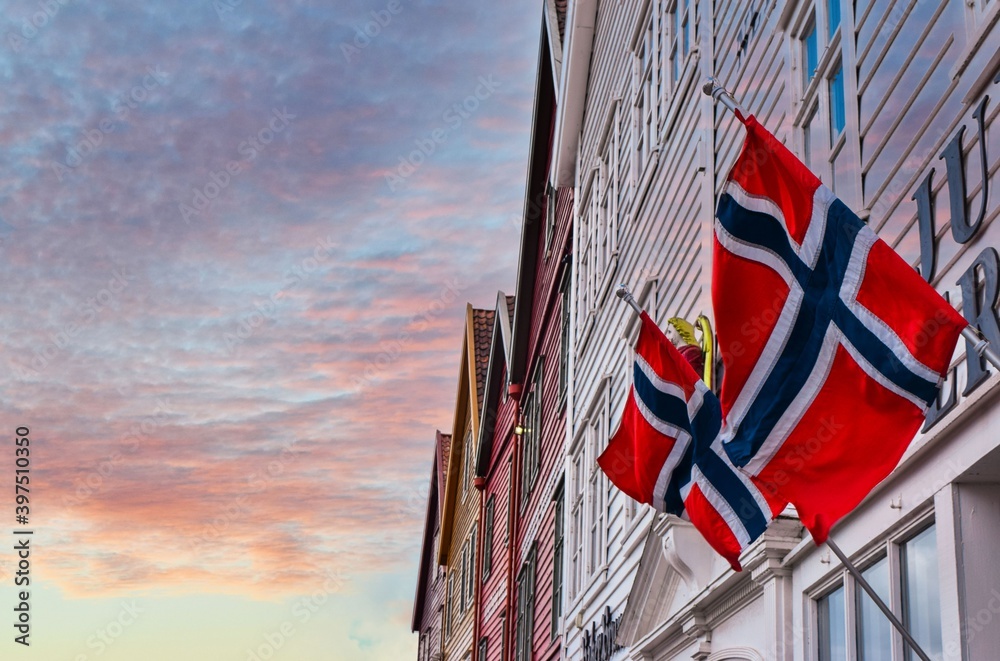 Φωτογραφία Norwegian flags waving in the wind on the wall of an old wooden house in Bergen against a beautiful sky at sunset