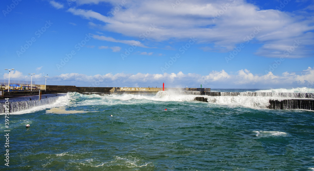 The harbor and the coast are overrun by very high, powerful waves. Marvel at the awe-inspiring power of nature - both magnificent and destructive. Sea is churned, spray and surf everywhere. 