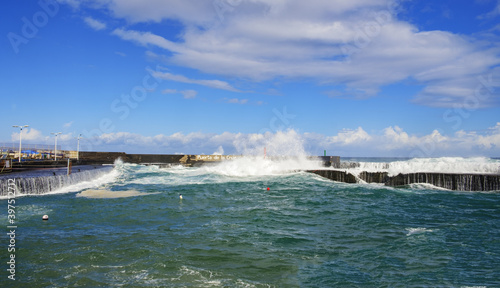 The harbor and the coast are overrun by very high, powerful waves. Marvel at the awe-inspiring power of nature - both magnificent and destructive. Sea is churned, spray and surf everywhere. 