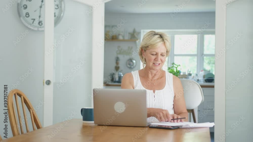 Retired senior woman at home in kitchen happy with sense of achievement at end of the day working on laptop relaxing and putting hands behind head - shot in slow motion Retired senior woman at home in kitchen happy with sense of achievement at end of the day working on laptop relaxing and putting hands behind head - shot in slow motion