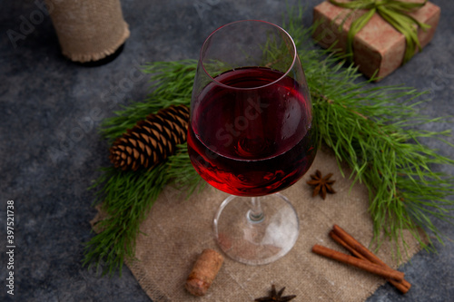 Red wine in a glass on a gray background with a bottle wrapped in jute or linen cloth on the background of a Christmas tree. The concept of the holiday, cozy Christmas, New year. Rustic style