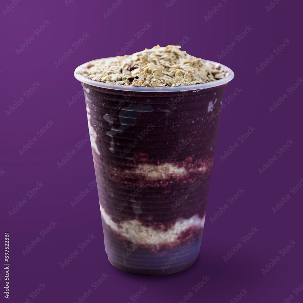 Brazilian frozen açai berry ice cream on a plastic cup with oatmeal flakes. isolated on purple background. Summer menu front view
