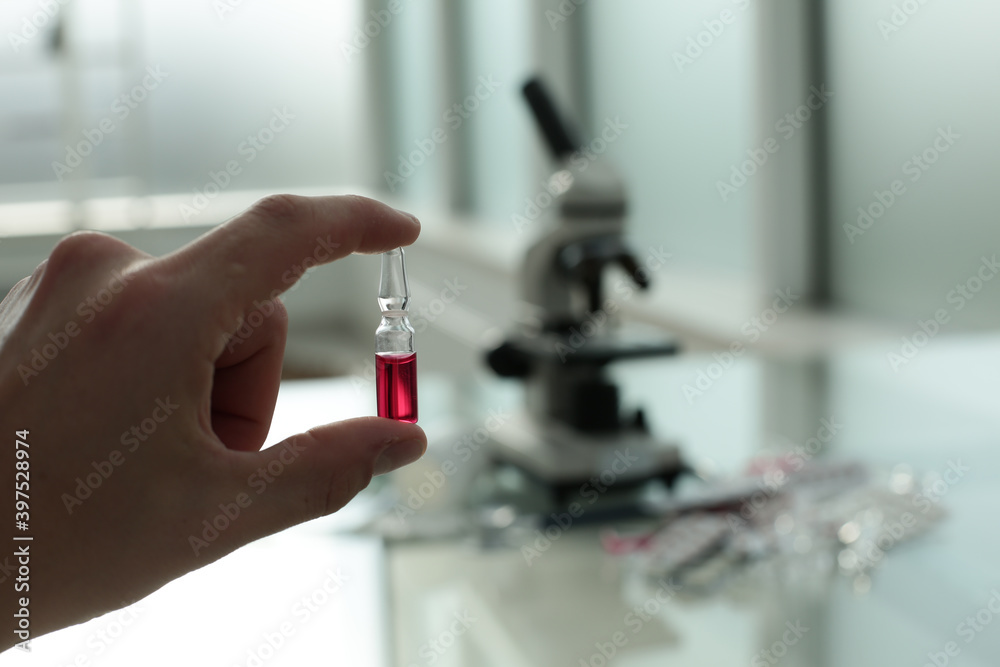 Doctor's hand holding a vaccine in his hands on the background of a glass table with medicines and a microscope Doctor's hand holding a vaccine in his hands on the background of a glass table with medicines and a microscope