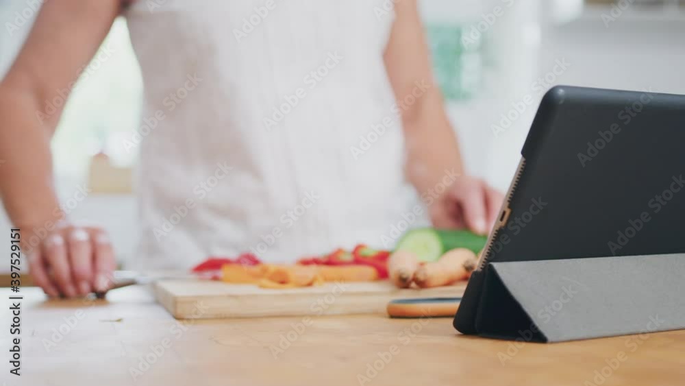 Close up of retired senior woman chopping vegetables for meal in kitchen following recipe on digital tablet - shot in slow motion