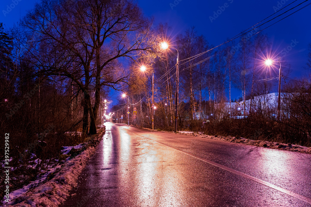 Winter street against a blue sky in the suburbs, illuminated by yellow lanterns in the evening