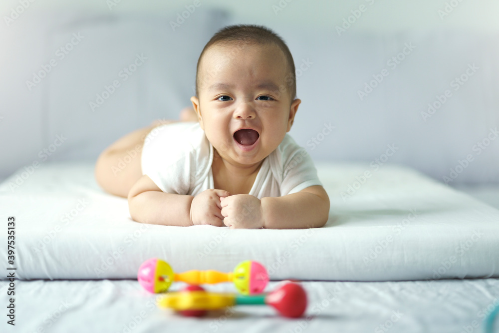Asian cute baby in white sunny bedroom. Newborn child relaxing on bed. Nursery for young children. Textile and bedding for kid. Family morning at home. New born kid during tummy time with toy. Asian cute baby in white sunny bedroom. Newborn child relaxing on bed. Nursery for young children. Textile and bedding for kid. Family morning at home. New born kid during tummy time with toy.