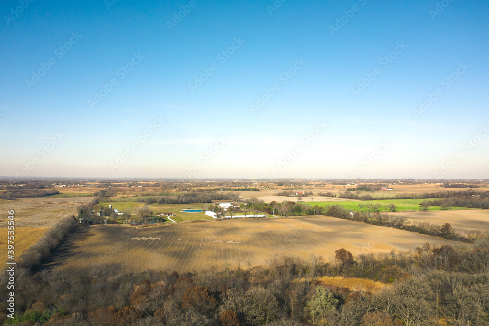 Fototapeta premium Beautiful aerial of farm fields in rural Wisconsin in autumn with patches of bare trees, barns and silos spread across the landscape beyond.