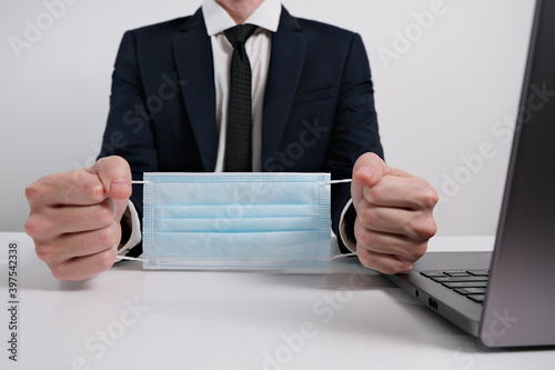 Businessman Sitting Behind a Table with Medical Mask, Hands Bound Like Handcuffs, Concept of Covid-19