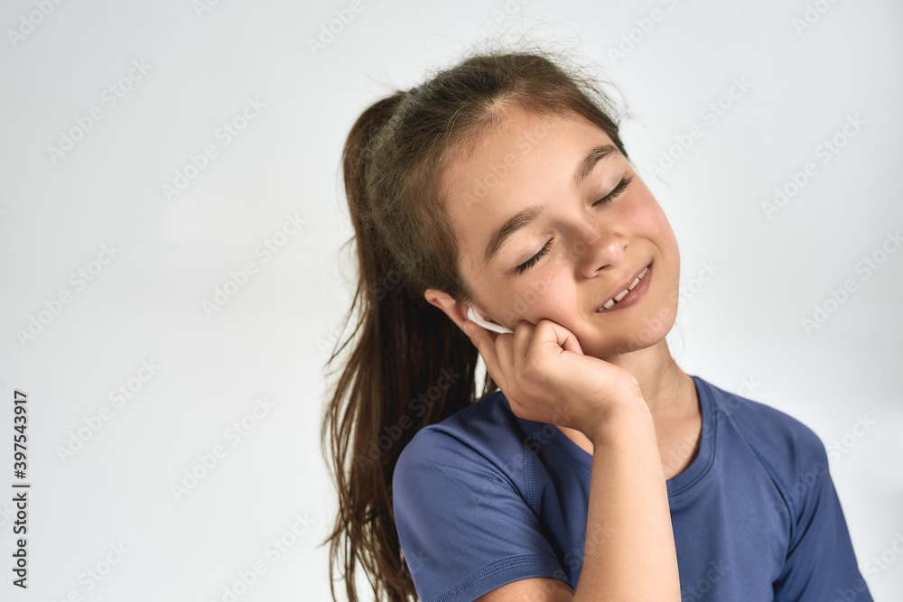 Portrait of little sportive girl child wearing earphones, listening to music, standing with eyes closed while posing isolated over white background Portrait of little sportive girl child wearing earphones, listening to music, standing with eyes closed while posing isolated over white background