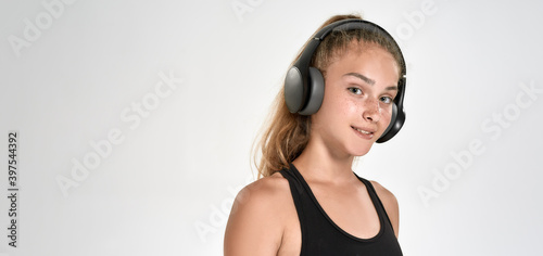 Portrait of cute sportive girl child wearing headphones, listening to music, looking at camera while posing isolated over white background