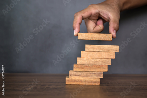 Close-up hand is placing wood block tower stacked in pyramid shape with caution to prevent collapse or crash concepts of financial risk management and strategic planning.