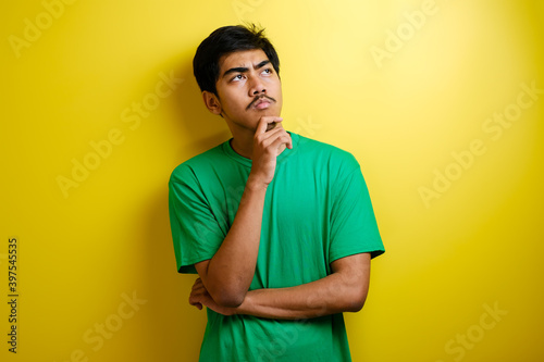 Asian man in green t-shirt thinking something, looking for good idea