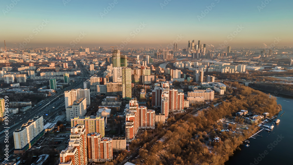 Fototapeta premium A big and beautiful city from a bird's eye view. City in the rays of the sun at sunset. Park, river, many houses and roads. Beautiful Moscow.