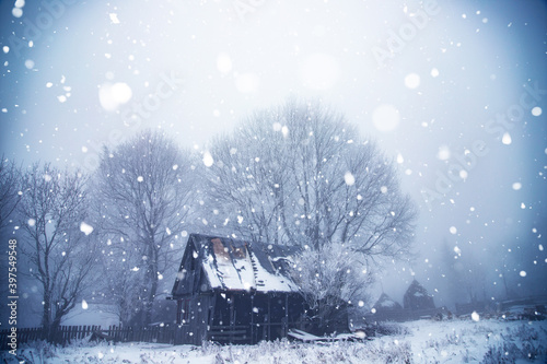 Dreamy winter landscape with small wooden hut in magic mist and snowfall.