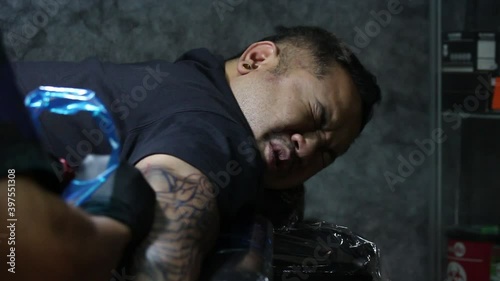 Close up shot of man face feeling pained from Tattooist making tattoo on his arm. facial expression of suffering