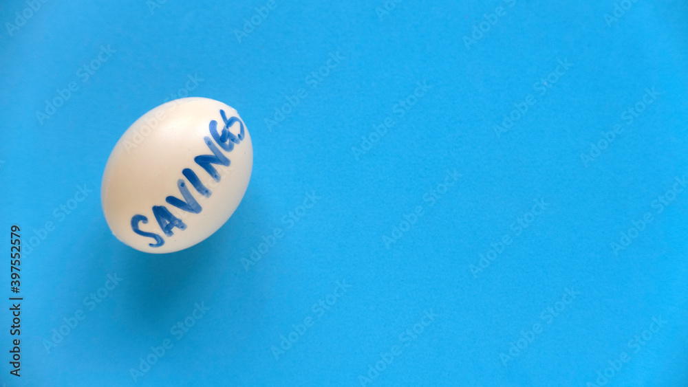 Savings concept. Top view of an egg written with SAVINGS on a blue background with copy space. Savings concept. Top view of an egg written with SAVINGS on a blue background with copy space.