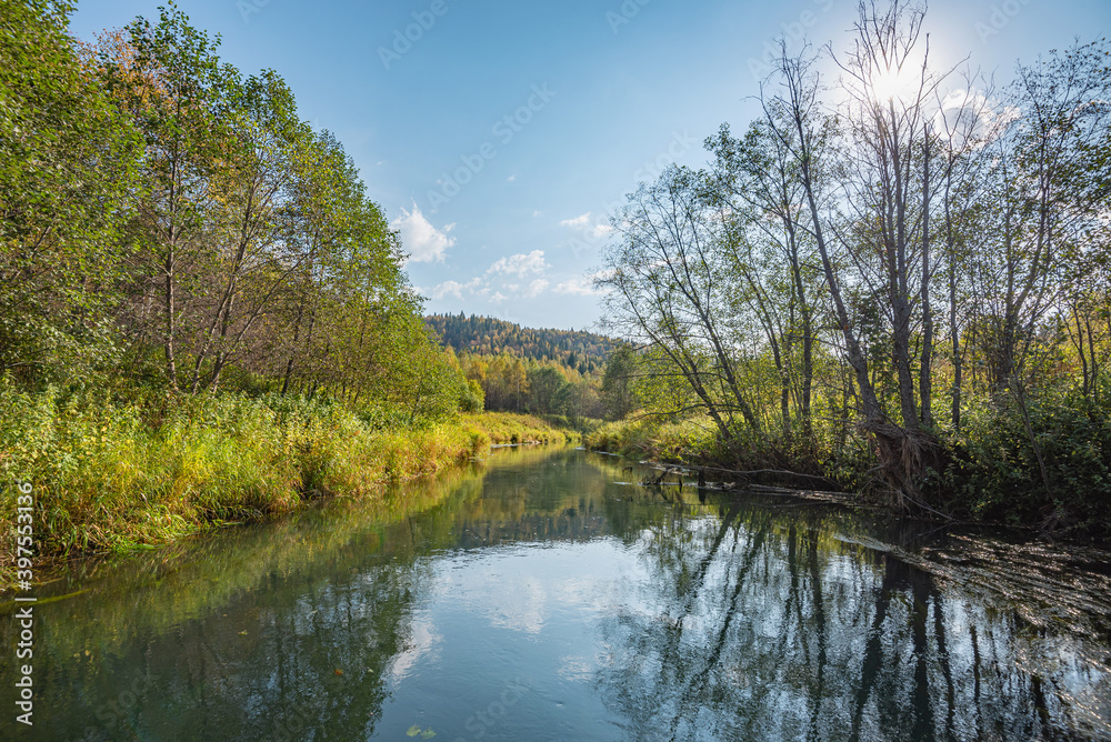 Autumn forest trees are reflected in the river water of the panoramic landscape. Blue sky with clouds. Autumn forest trees are reflected in the river water of the panoramic landscape. Blue sky with clouds.