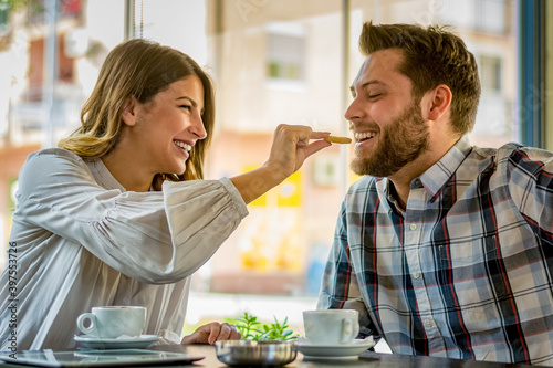 Cute couple having breakfast in cafe together. Woman feeding her boyfriend with biscuit. Romantic couple drinking coffee