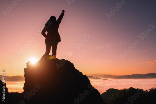 The silhouette of a woman standing on the top of the mountain at sunrise. Success concept.