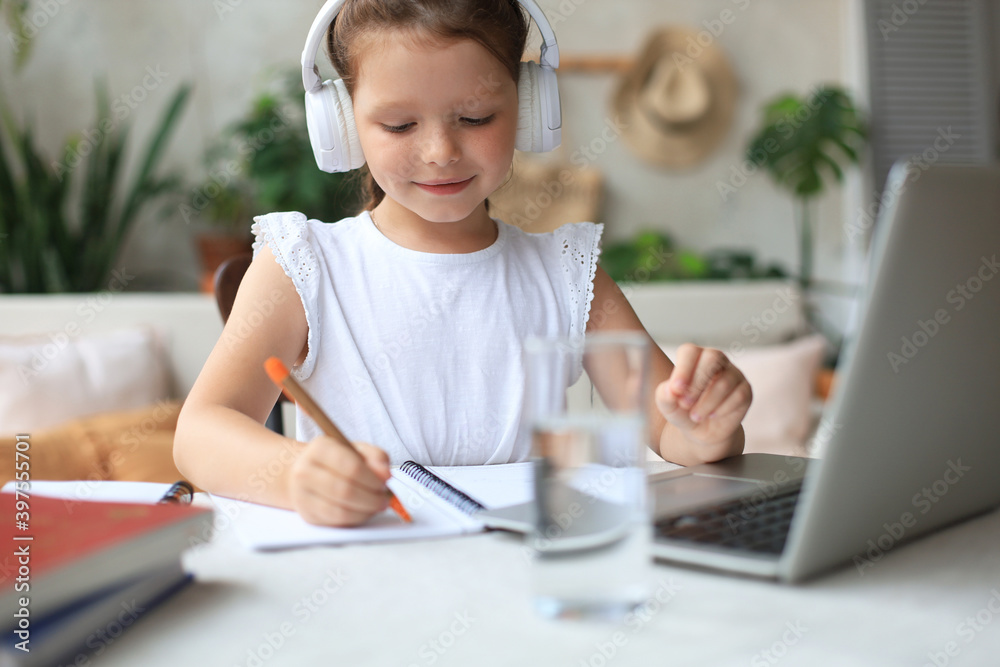 Smiling little girl in headphones handwrite study online using laptop at home, cute happy small child in earphones take Internet web lesson or class on PC. Smiling little girl in headphones handwrite study online using laptop at home, cute happy small child in earphones take Internet web lesson or class on PC.