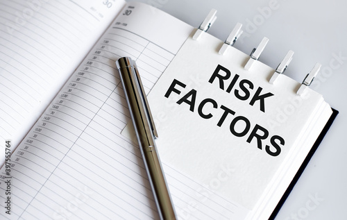 text RISK FACTORS on the short note texture background with pen