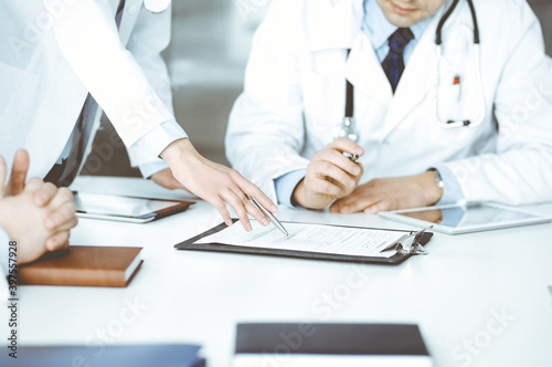 Group of unknown doctors are sitting at the desk and discussing medical treatment  using a clipboard  close-up. Team of physicians at work in a clinic. Medicine and healthcare concept