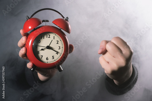 Manager is showing an alarm clock and is shaking by his fist close up. The boss scolds for being late for work. photo