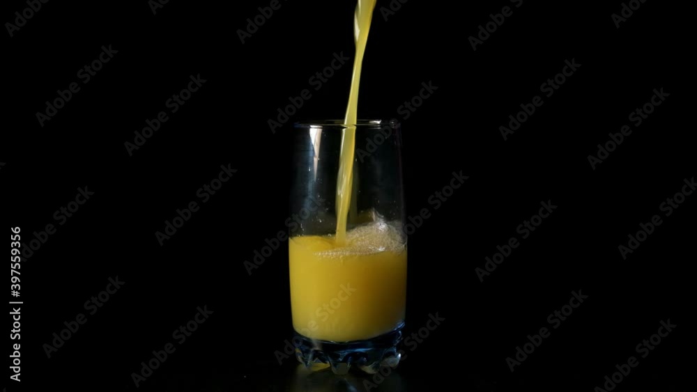 Pure juice. Super slow motion shot of pouring orange juice into a transparent glass against black background. Healthy drink, vitamins, fruits. Pure juice. Super slow motion shot of pouring orange juice into a transparent glass against black background. Healthy drink, vitamins, fruits.