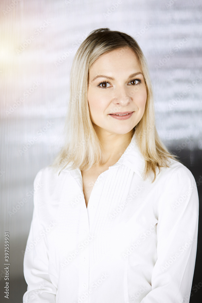 Friendly adult business woman standing straight. Business headshot or portrait in sunny office