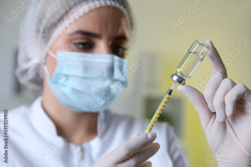 Doctor filling syringe with medication in clinic, focus on hands. Vaccination and immunization