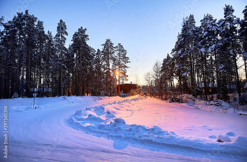 Winter landscape. The road was covered with snow. Village in the forest. The sun goes down.