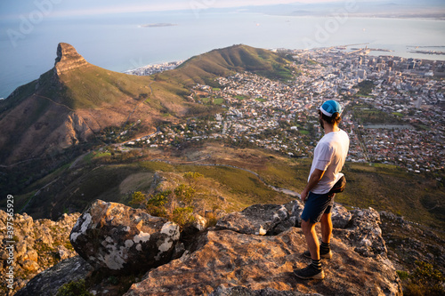 A fit trail runner looking down on Cape Town from the top of the mountain with a view of the city and the ocean.