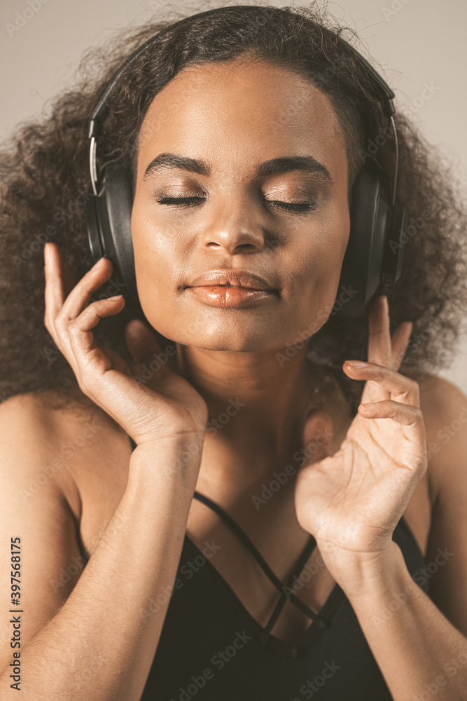 Fototapeta premium Close up. Capture away by music young African-American girl listening music with eyes closed wearing headphones, isolated on grey background, emotionally move, have fun. 