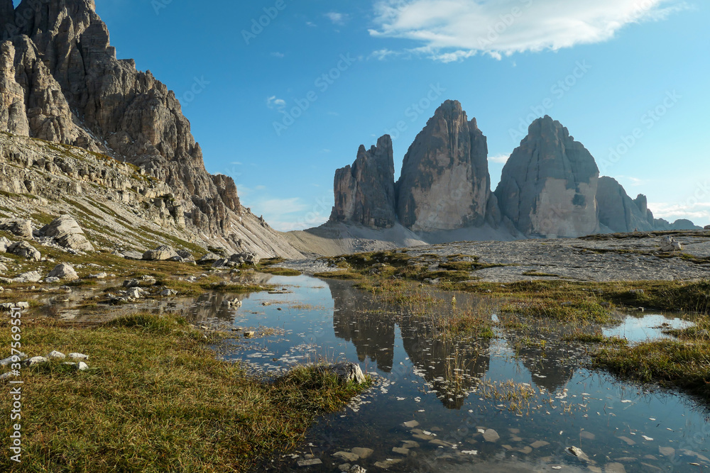 A panoramic view on the famous Tre Cime di Lavaredo (Drei Zinnen), mountains in Italian Dolomites. The mountains are reflecting in small paddle. Desolated and raw landscape. Natural phenomenon
