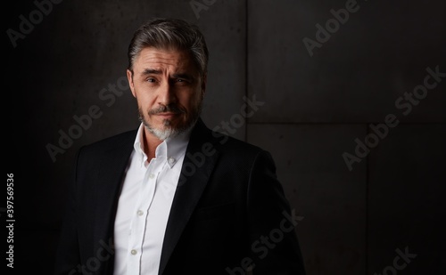 Business portrait of older man in 50s with gray hair against dark background. Businessman, copy space.