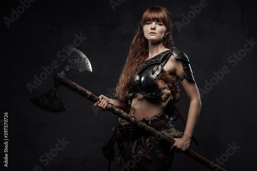 Cuadro en lienzo Armed with huge axe and armoured woman viking with long brown hairs poses in dark background