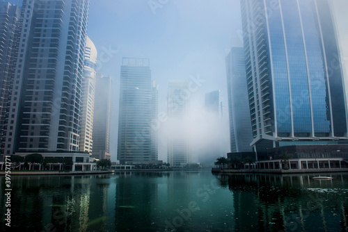 A beautiful view of modern skyline through fog in the morning at an upscale community in Dubai. Modern skyscrapers with lake view during misty weather. photo