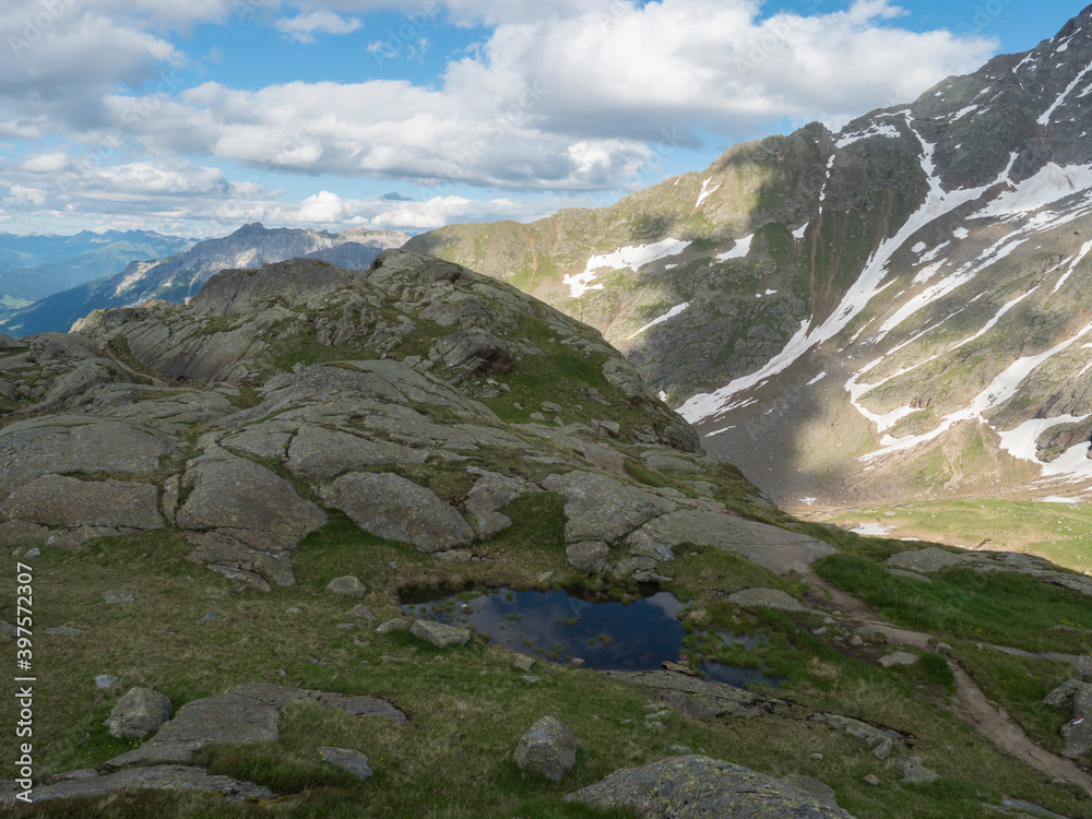View from Bremer Hutte with lake from melting snow tongues and snow-capped moutain peaks, lush green meadow, blue sky backgound. Late spring sunny afternoon, vibrant colors