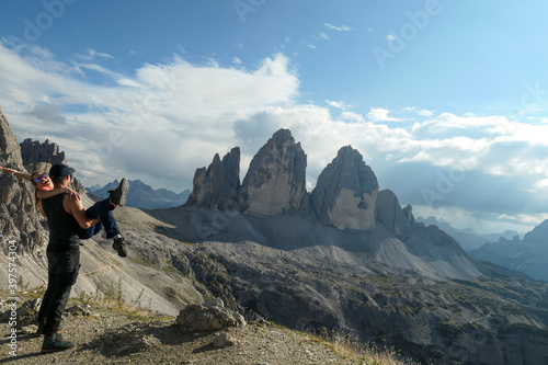A man holding a woman in his arms on top of Sextner Stein and enjoying the view on the famous Tre Cime (Drei Zinnen) in Italian Dolomites. Desolated and raw landscape, full of lose stones. Love © Chris