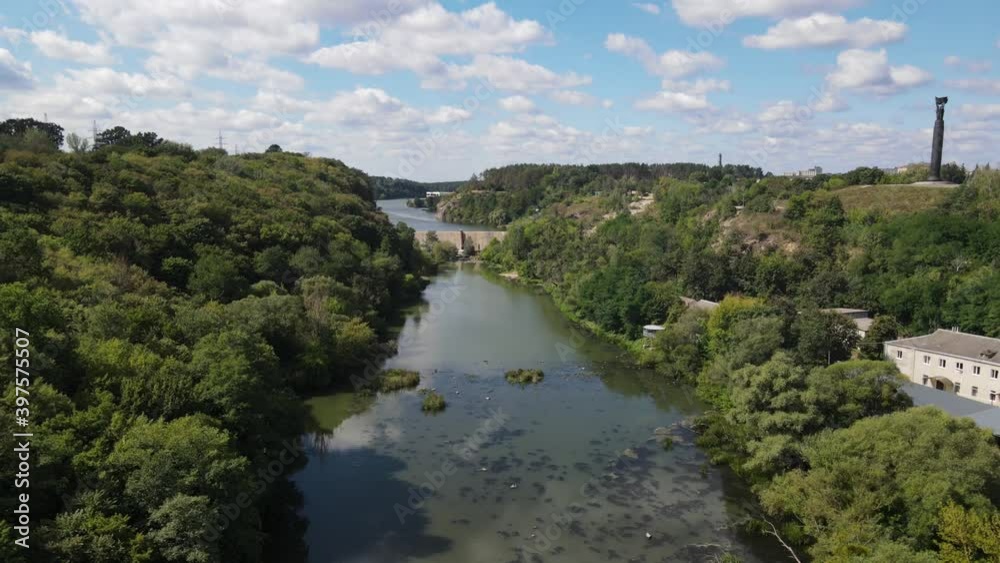 River. There are stone cliffs and rocks around the water. Trees grow densely near the rocks. Residential buildings are visible in the background. River. There are stone cliffs and rocks around the water. Trees grow densely near the rocks. Residential buildings are visible in the background.