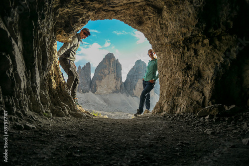 A couple standing in front of a cave, with the view on the Tre Cime (Drei Zinnen) in Italian Dolomites. They is enjoying the peaceful scenery. Steep and sharp mountain peaks. Serenity and meditation